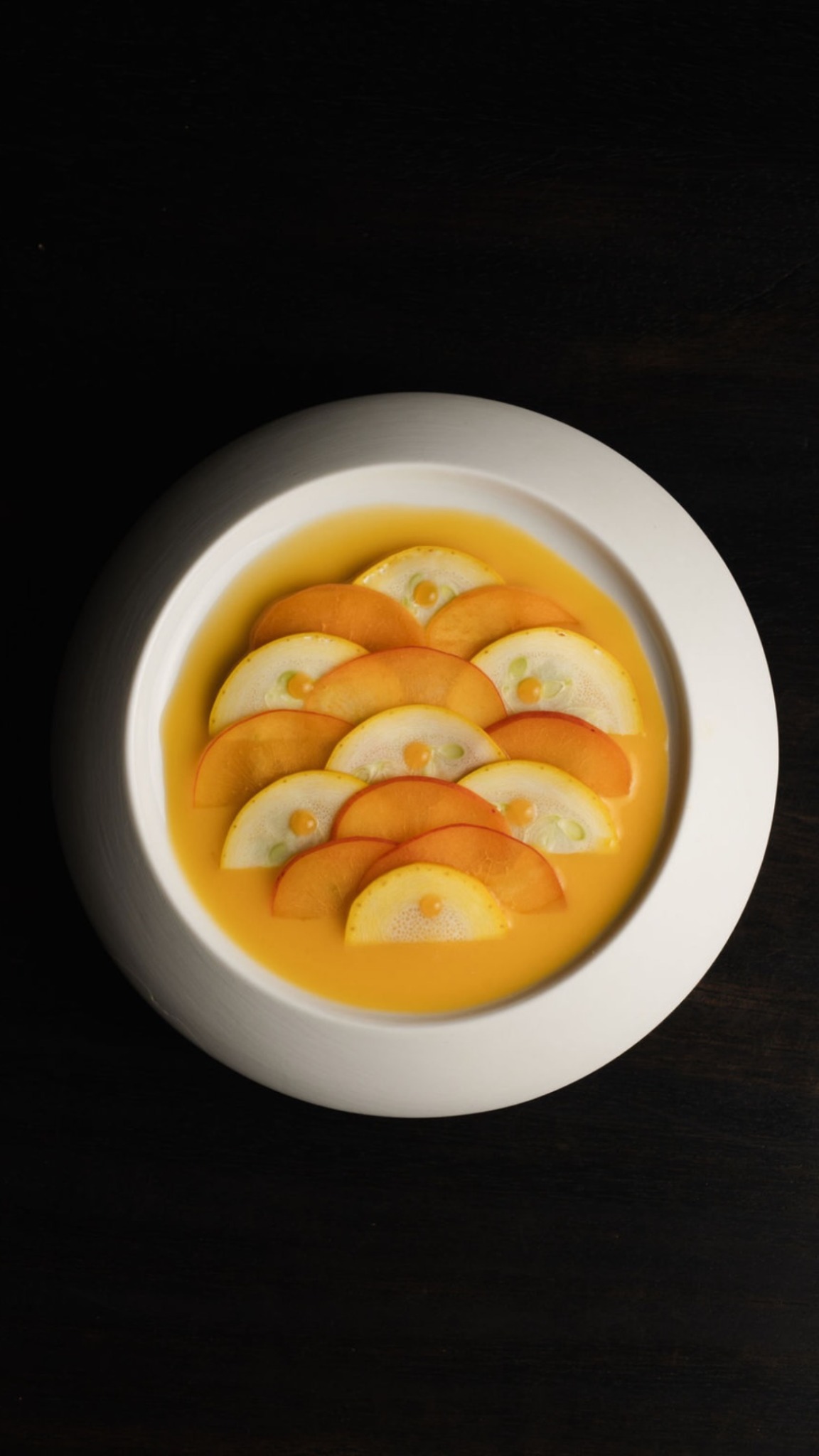 A carefully composed plate with fruit and a golden sauce
